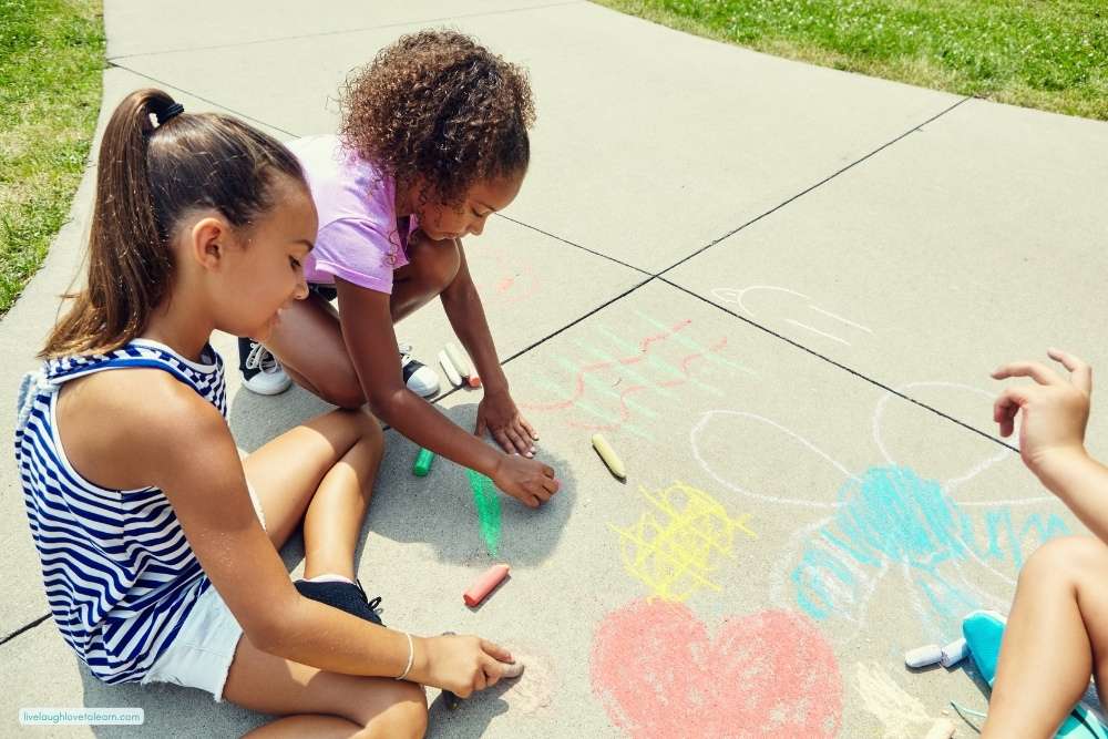 Elementary students drawing colorful chalk art on a sidewalk during an end-of-year outdoor school activity.