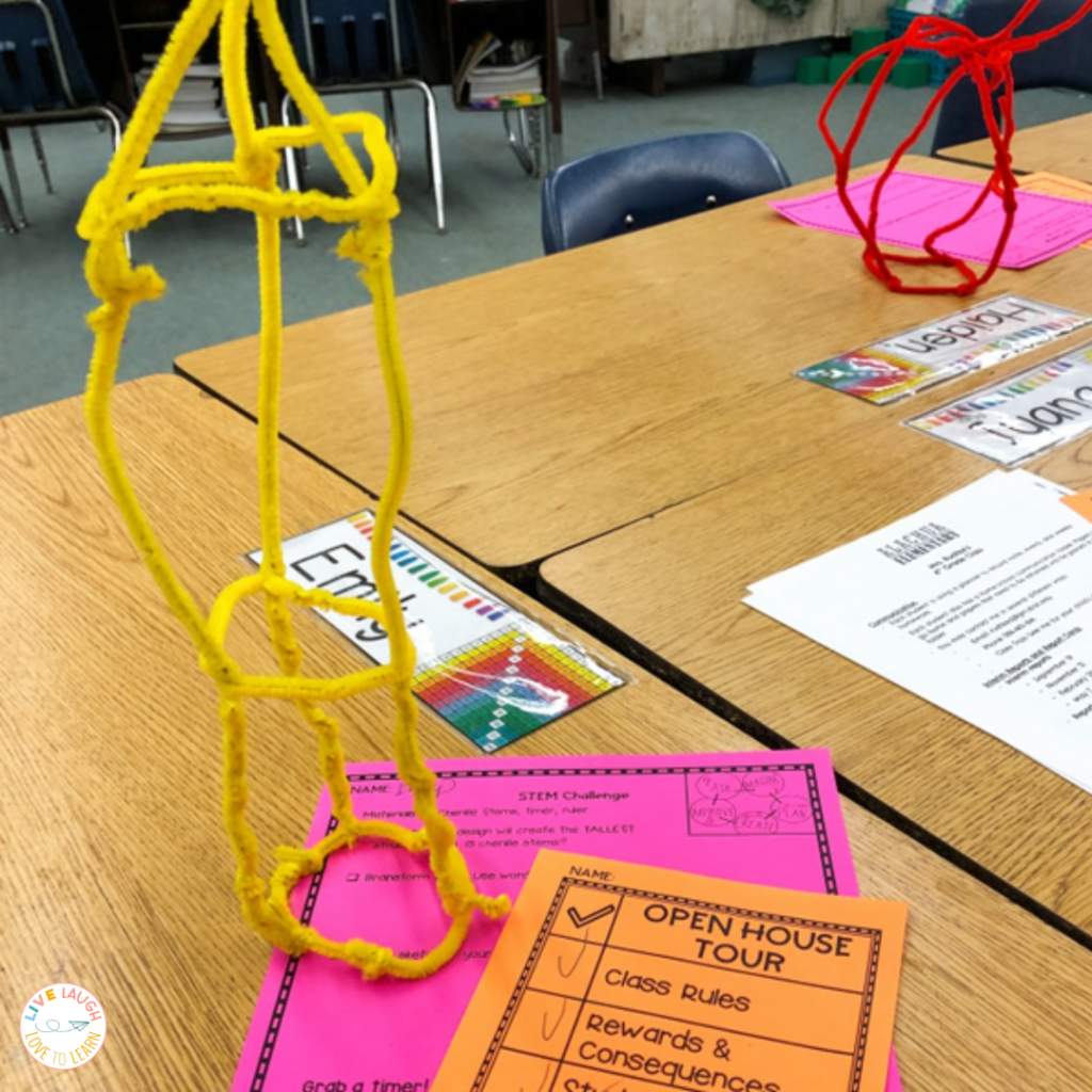A photo of a classroom open house with several desks with papers and chenille stem towers on top of the desks.