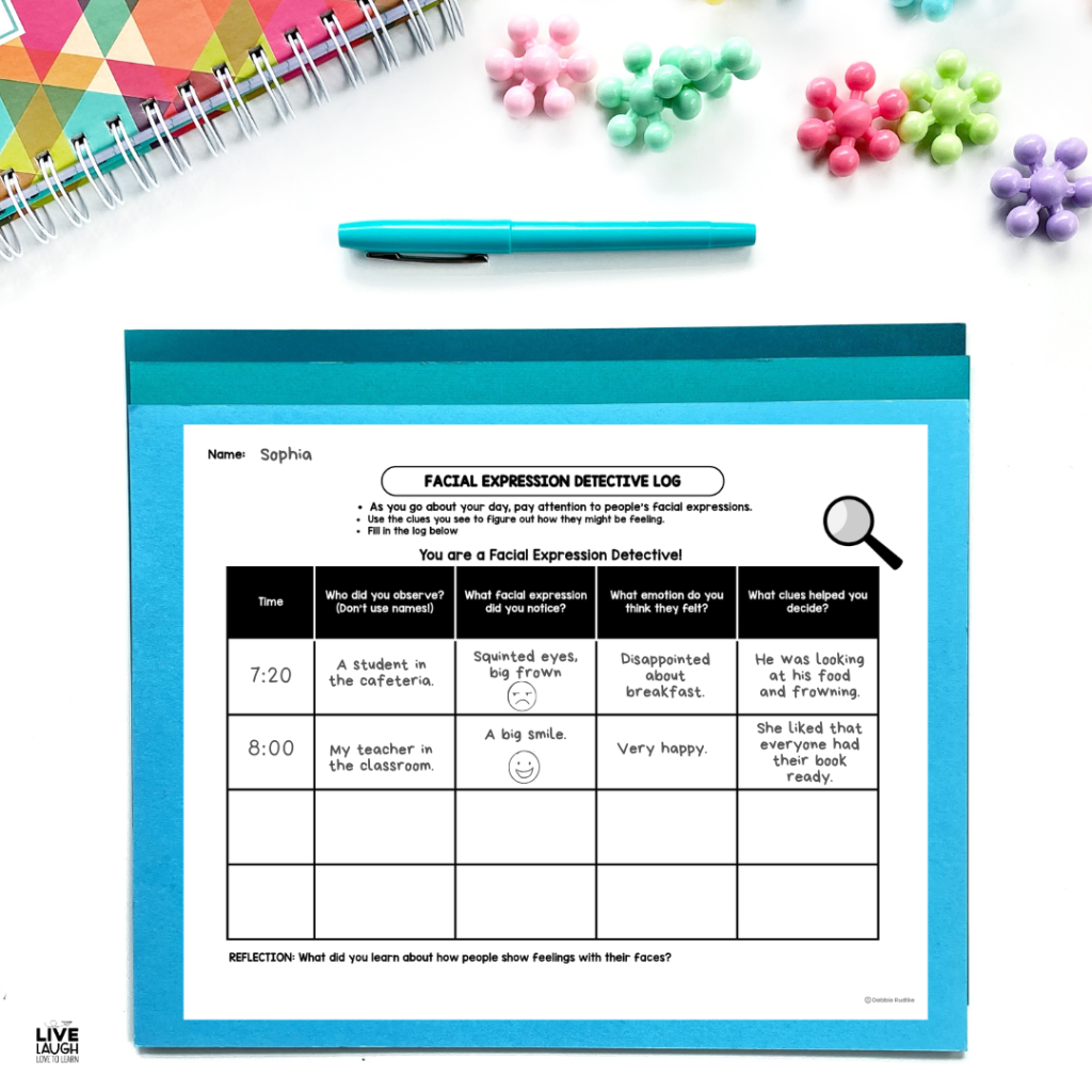 A student worksheet titled "Facial Expression Detective Log" is filled out and displayed on a blue folder with a pen and colorful push pins nearby. The activity prompts students to observe others’ facial expressions, record what they notice, and infer emotions based on visual clues. The log includes columns for time, observation, expression, emotion, and evidence, helping students practice non-verbal communication skills.