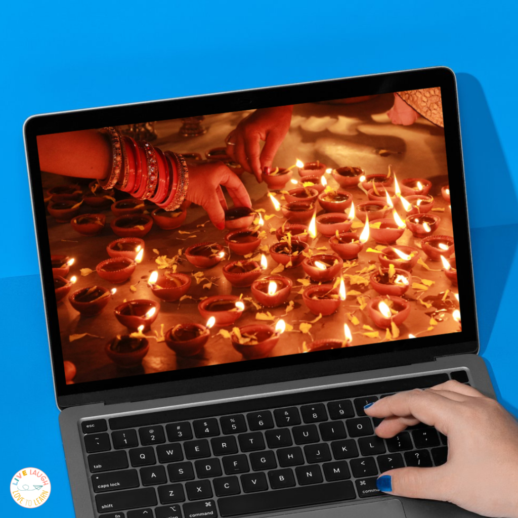A laptop screen displaying a close-up photo of Diwali celebration lights, with hands arranging rows of glowing oil lamps called diyas. The warm light contrasts with the blue background, symbolizing cultural learning during holidays around the world activities.