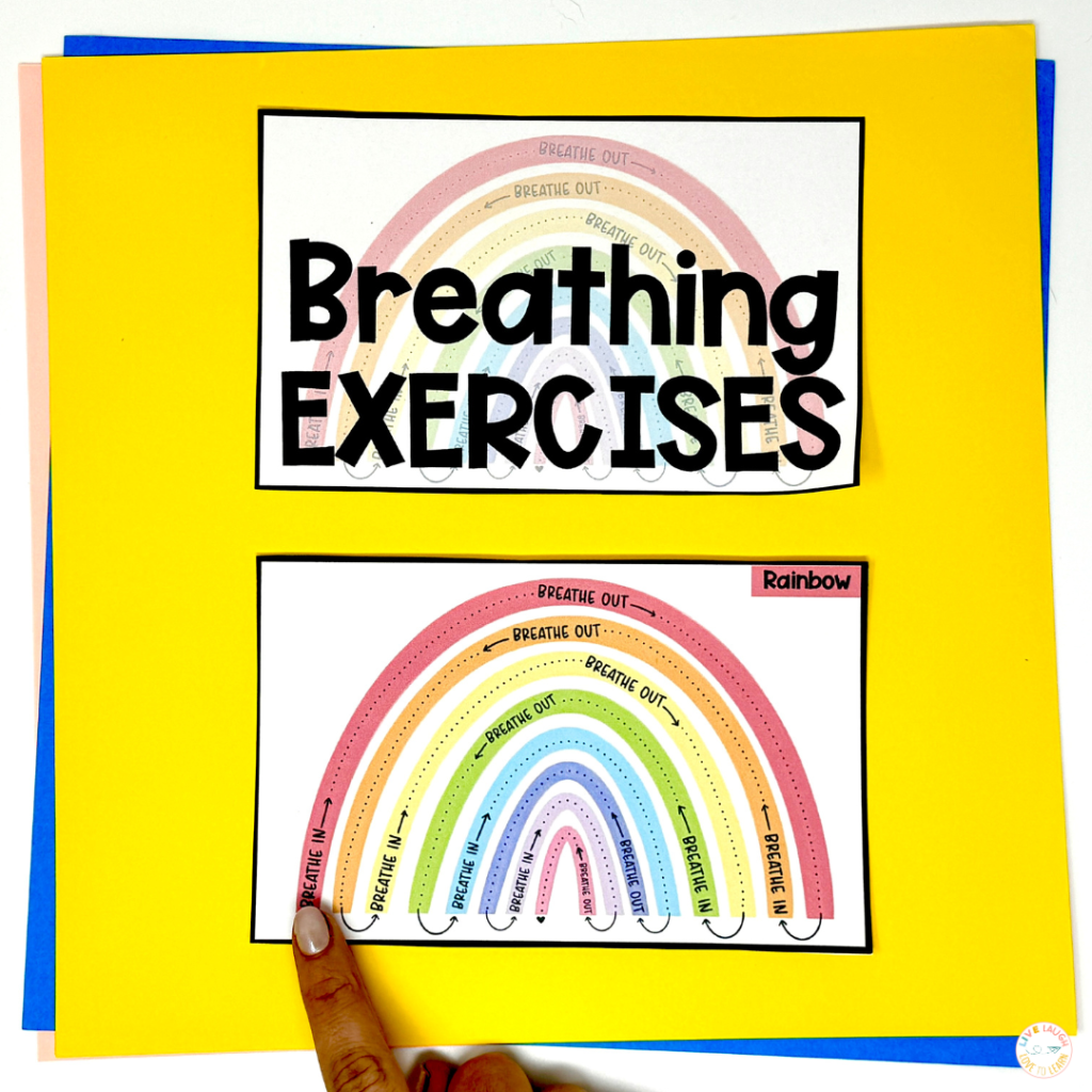 Mindfulness activities for kids breathing exercises visual showing a rainbow-shaped guided breathing graphic with ‘breathe in’ and ‘breathe out’ prompts. A hand points to the starting spot, with colorful paper stacked underneath.