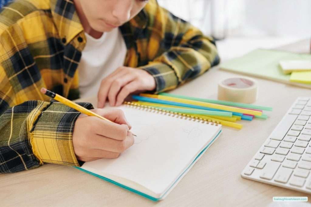 Student writing in a notebook during a reflection in STEM with colorful straws and tape on the desk