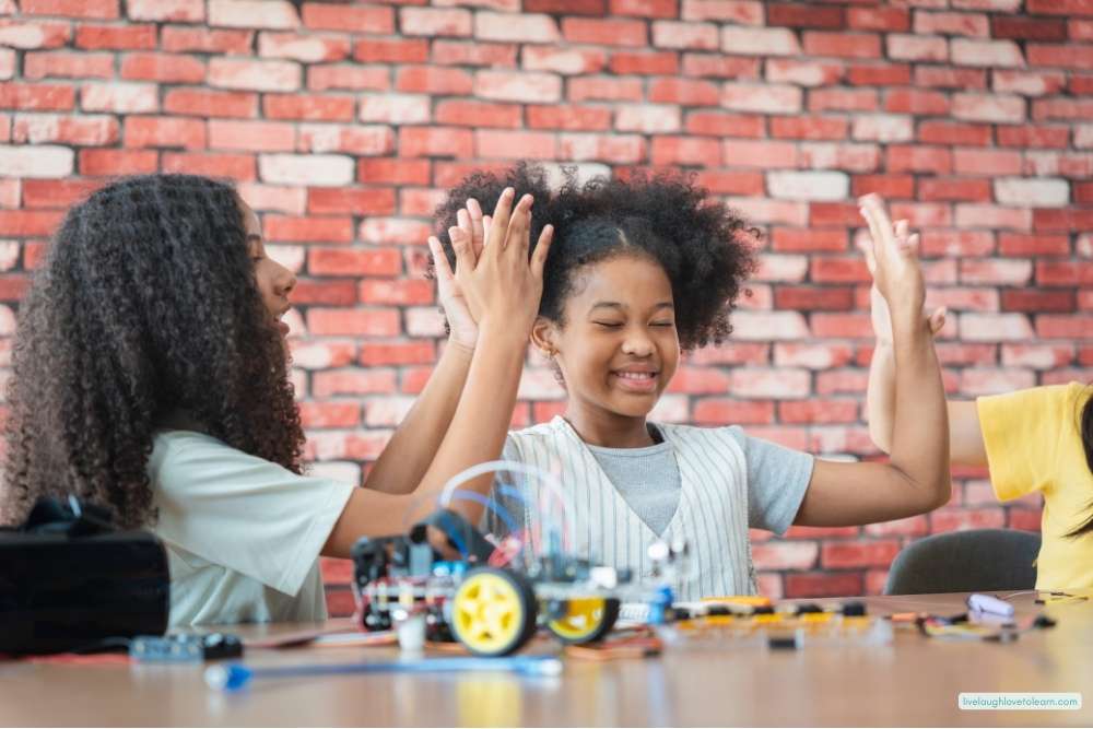 Two elementary students celebrating during a STEM engineering challenge with a robot on the table