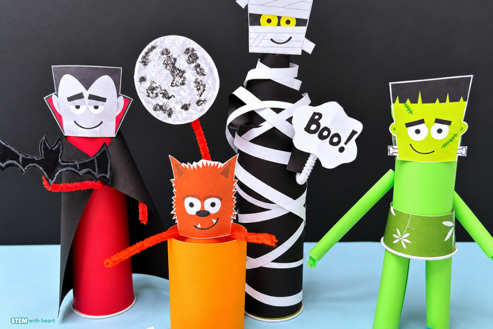 Four completed Halloween STEM monster designs made from paper cups, construction paper, and pipe cleaners, including a vampire, mummy, werewolf, and Frankenstein.